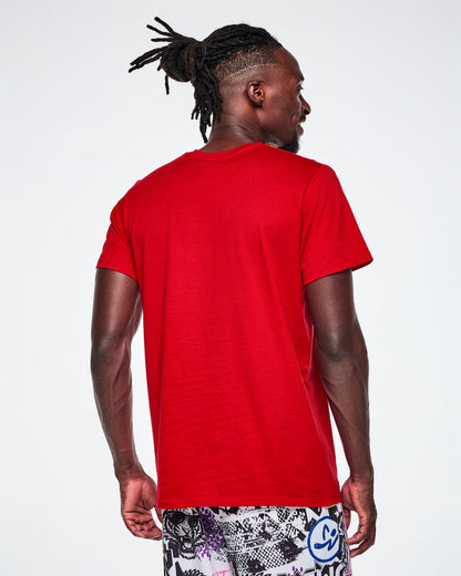 A male model wearing a red short-sleeve tee and multi-colored pants.
