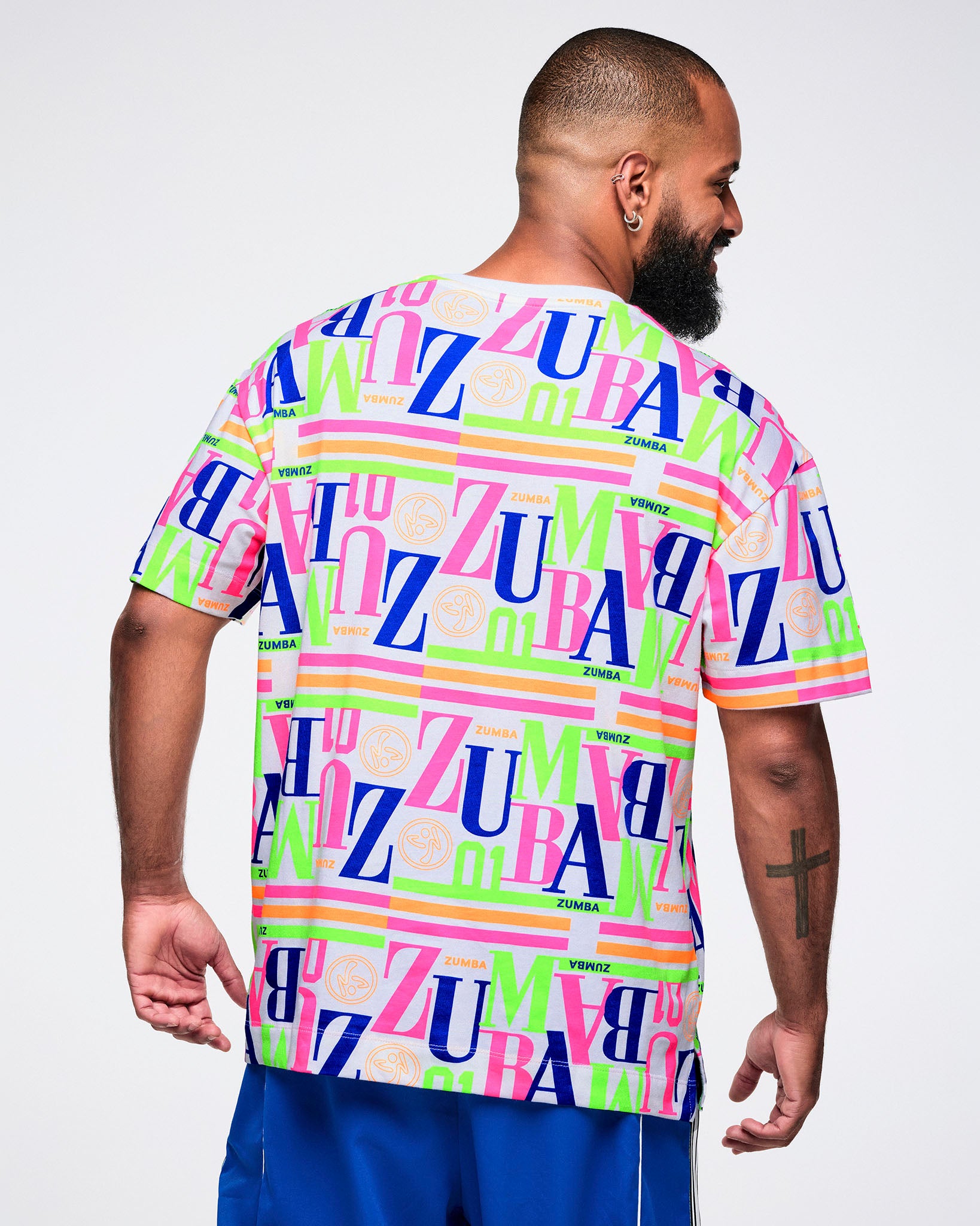 Back view of a male model wearing a colorful 'Zumba' t-shirt on a white background.