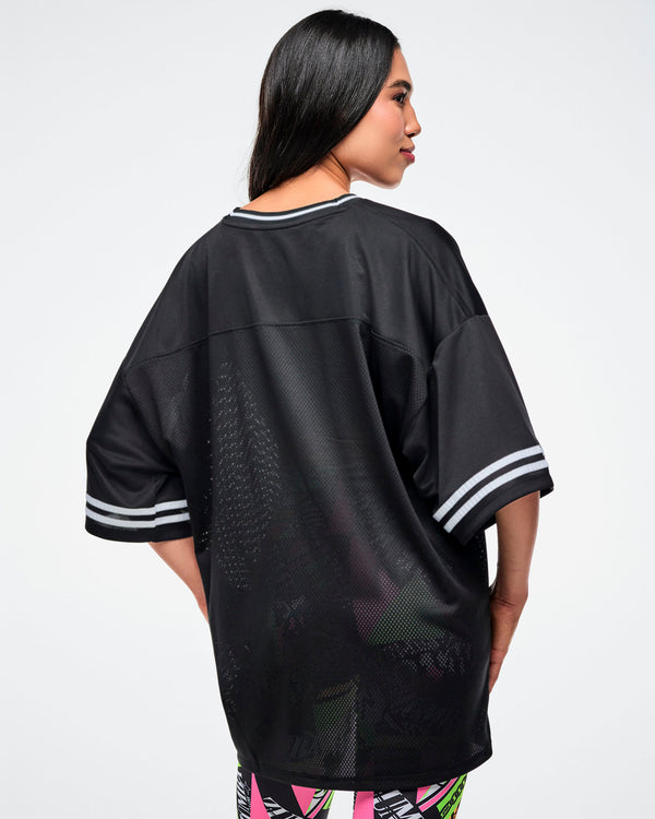Back view of a female model wearing a black Zumba jersey paired with matching patterned leggings on a white background.