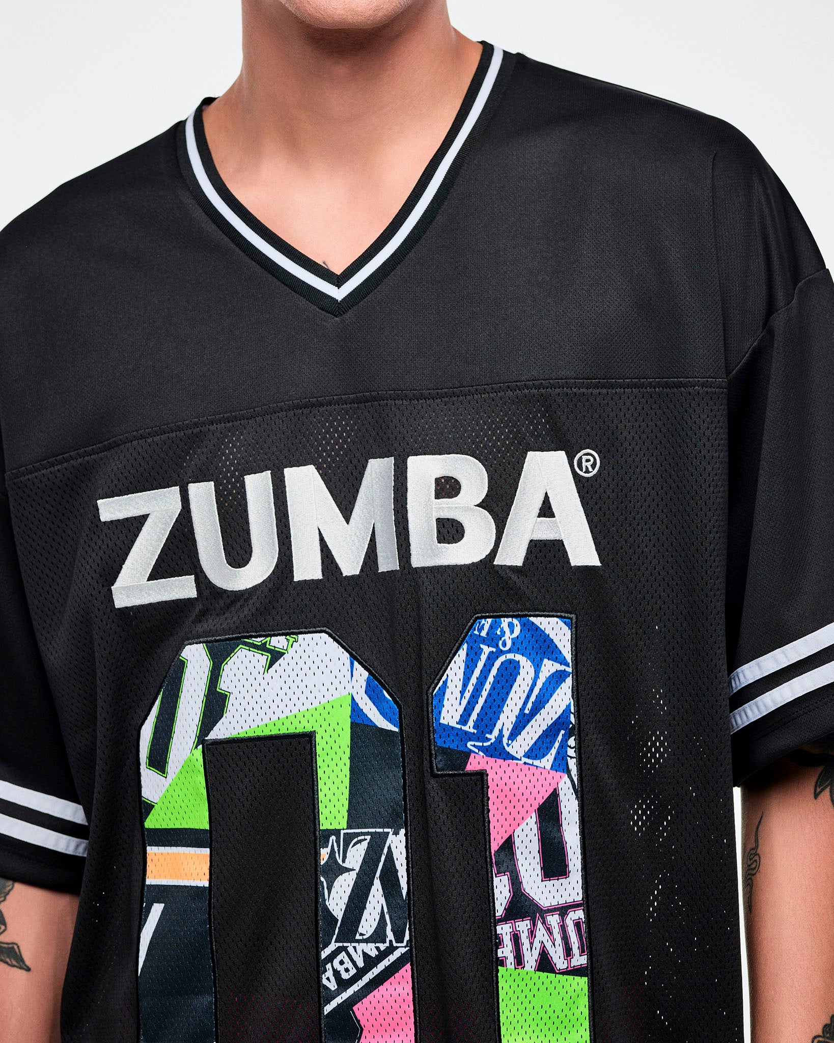 Close-up of a male model wearing a black Zumba jersey with silver “ZUMBA” text and a large colorful patterned “01."