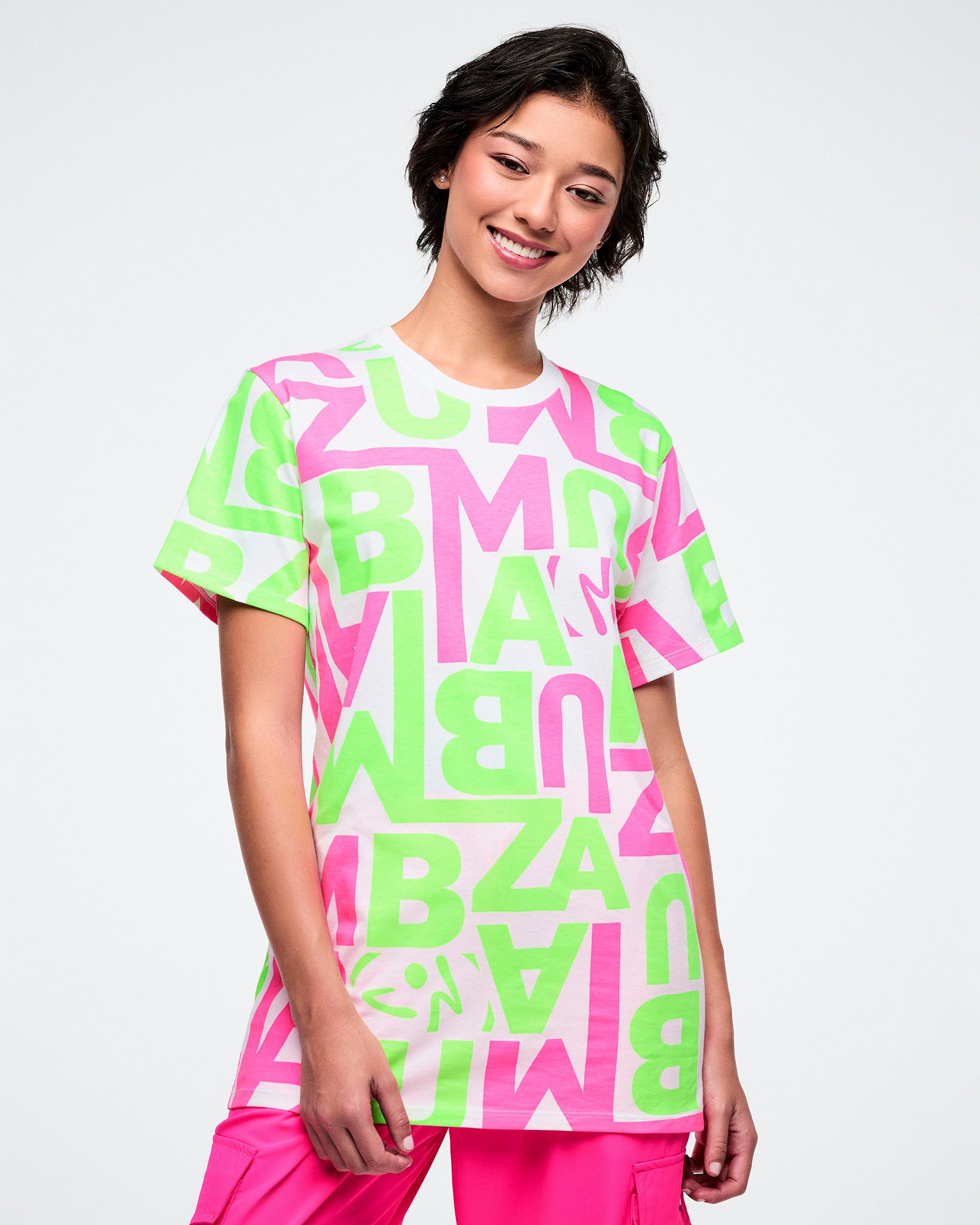 Female model wearing a bright neon green and pink patterned white tee paired with pink pants.