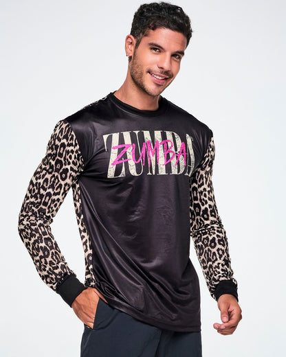 A male model wearing a black long-sleeve top with tan leopard-print sleeves and a pink and white Zumba text across the chest, paired with black pants.