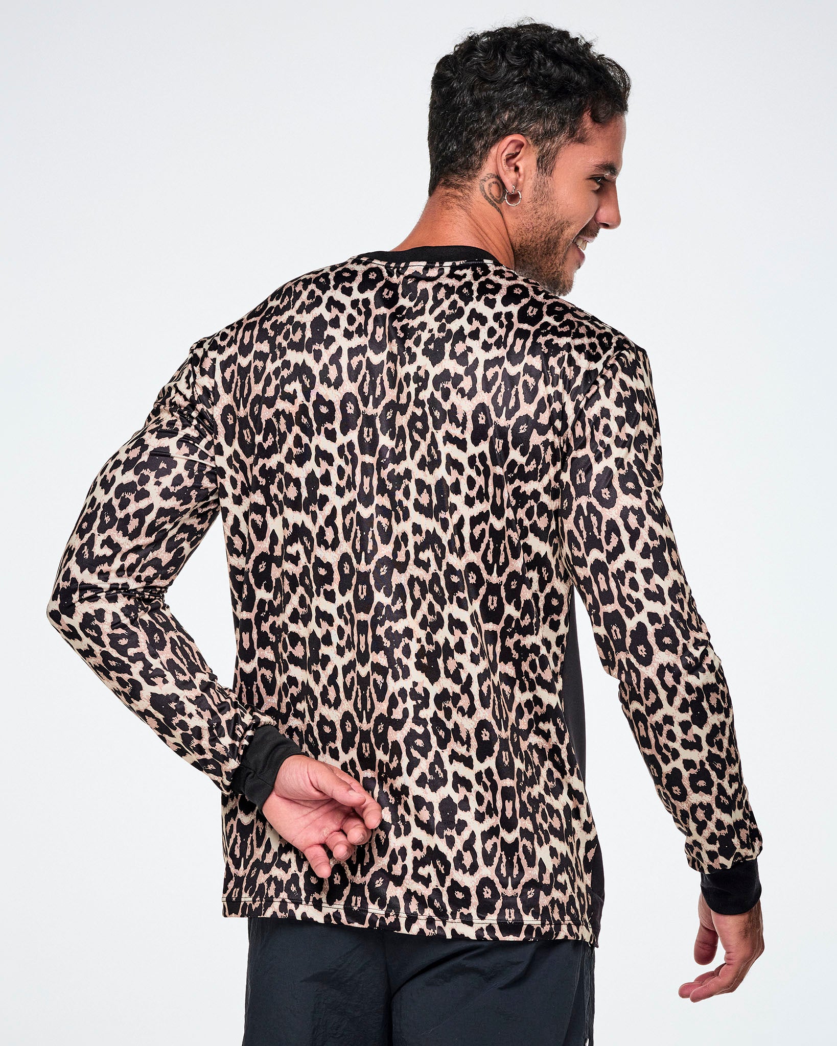 A male model, shown from behind, wearing a full backed, tan leopard-print long-sleeve top with black cuffs and a black collar, paired with bright pink snake-skin patterned shorts.