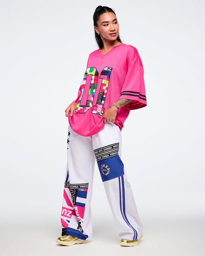 Female model wearing a pink mesh top and white pants with colorful patterns.