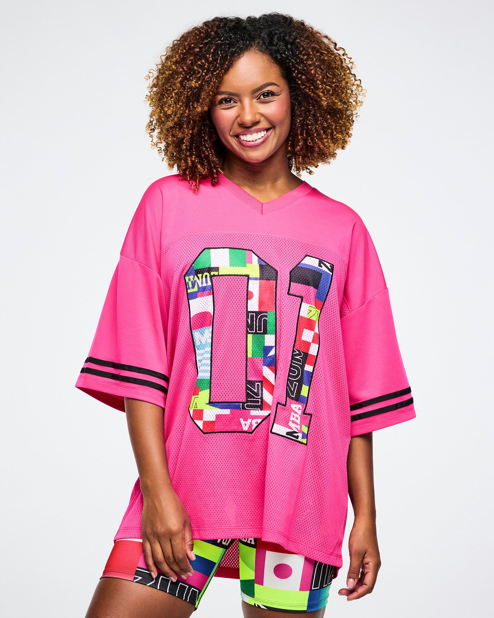 Female model wearing a pink mesh jersey with colorful designs on a white background.