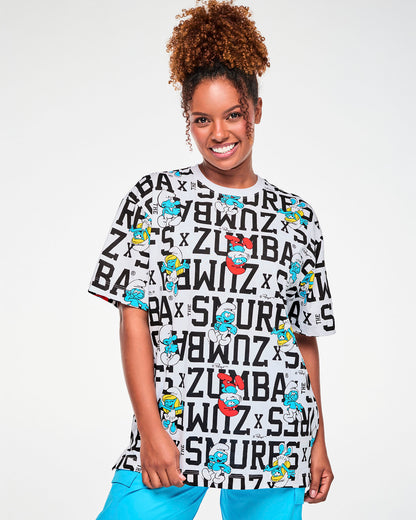 Female model in a white oversized crew neck top covered in bold black varsity 'ZUMBA x THE SMURFS' text, with Papa Smurf, Smurfette, and other Smurfs, paired with aqua blue cargo pants.