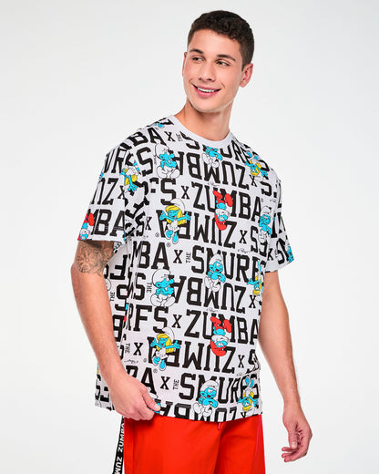 Male model in a white oversized crew neck top with an all-over print of bold black varsity 'ZUMBA x THE SMURFS' text and Smurfs characters, including Papa Smurf and Smurfette, paired with red pants.