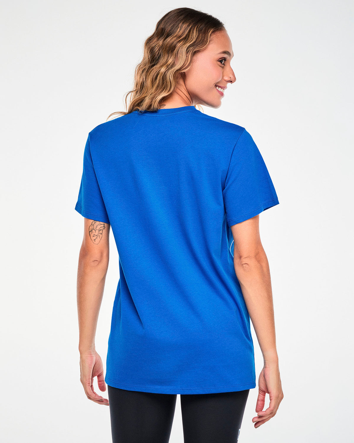 Shown from the back, a female model in the blue Smurfs graphic tee, showing the plain back and easy, relaxed fit through the body.