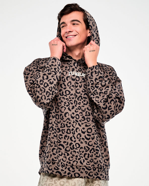 Male model pulling up the hood of a brown leopard print pullover sweatshirt with both hands, showing the roomy sleeves and dropped shoulders.