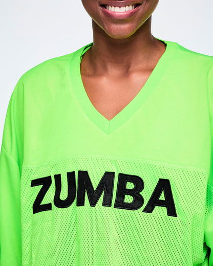 Close-up of a female model wearing a bright green V-neck mesh jersey with large black 'ZUMBA' lettering across the chest.