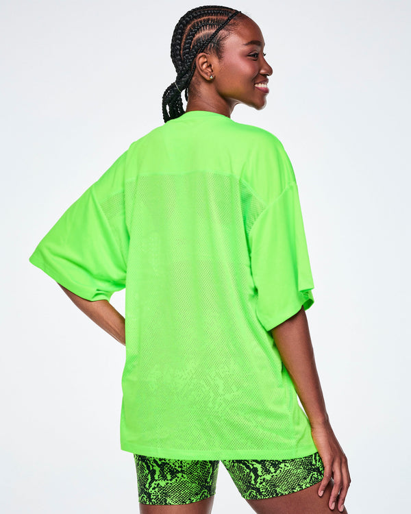 Back view of female model wearing an oversized bright green mesh V-neck top, paired with snake-skin patterned high-waisted biker shorts.