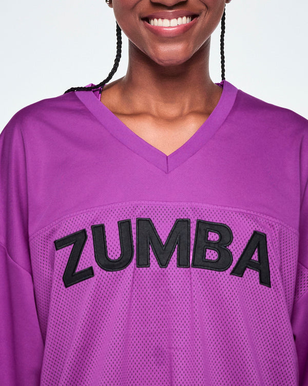 Close-up of a female model wearing a purple V-neck mesh jersey with large black 'ZUMBA' lettering across the chest.
