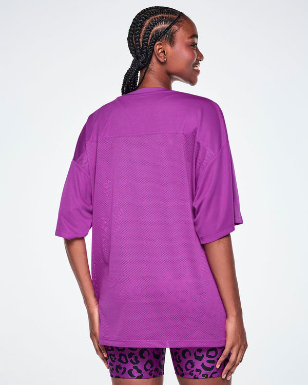 Back view of a female model wearing an oversized purple mesh V-neck top, paired with purple leopard print high-waisted biker shorts.