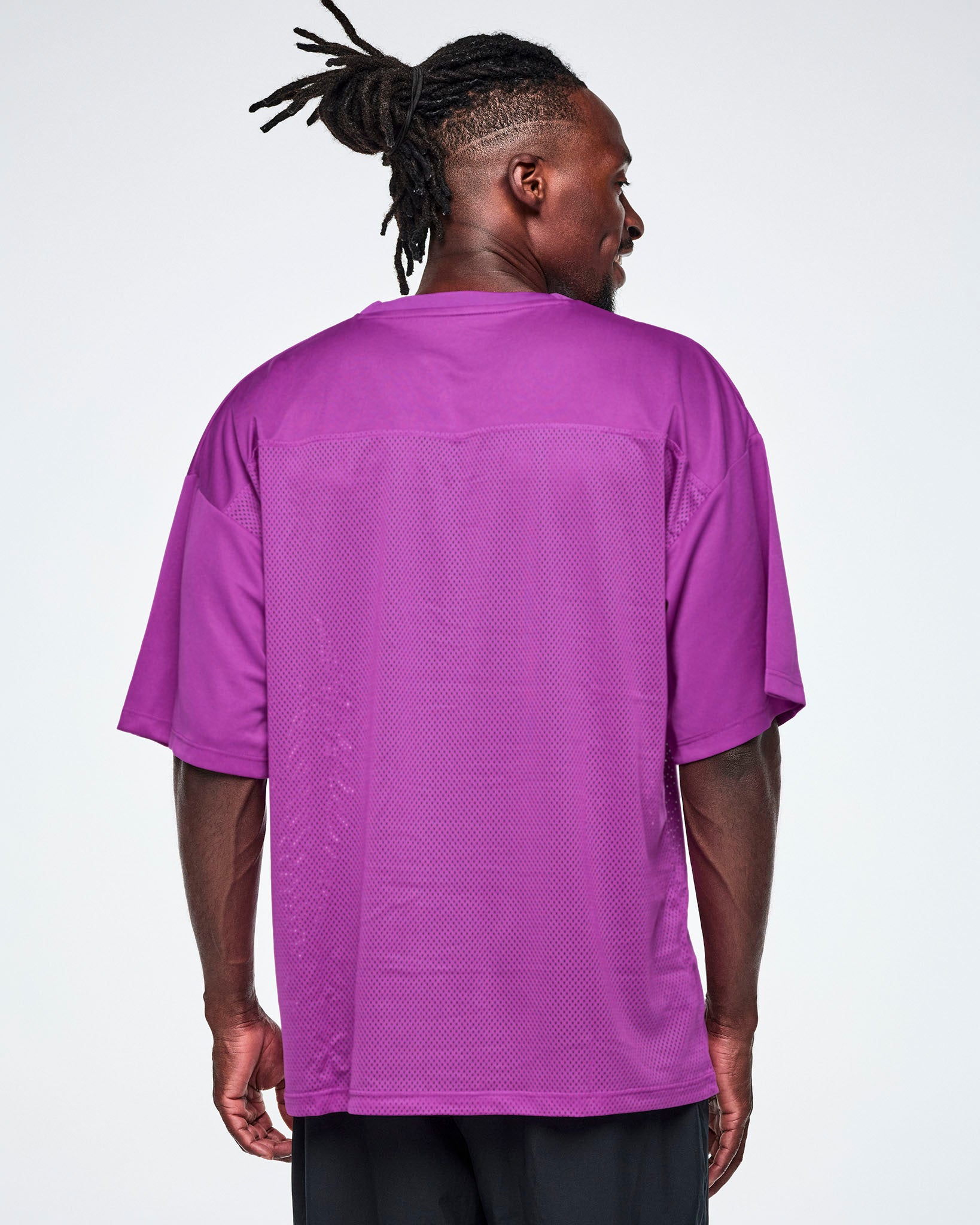 Back view of a male model wearing an oversized purple mesh V-neck top, paired with black pants.