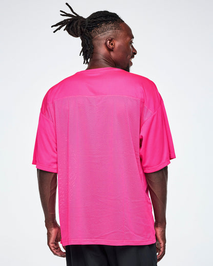 Back view of a male model wearing an oversized bright pink mesh V-neck top, paired with black pants.