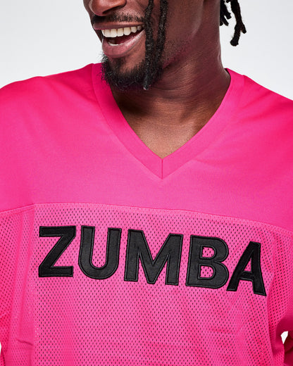 Close-up of a male model wearing a bright pink V-neck mesh jersey with large black 'ZUMBA' lettering across the chest.
