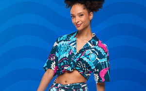 Banner showing a female model against a bright blue wavy background, highlighting a bold tropical matching set. 